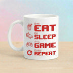 White ceramic "Eat Sleep Game Repeat" pixel art gaming mug with red Japanese kanji text on wooden surface with soft pink-blue pastel background – Japanese aesthetic gamer gift mug
