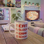 Eat Sleep Game Repeat" ceramic mug with steaming drink on wooden gaming desk in front of RGB PC setup, white keyboard, Funko Pops and cozy pixel game on monitor – cozy gamer room aesthetic gift mug